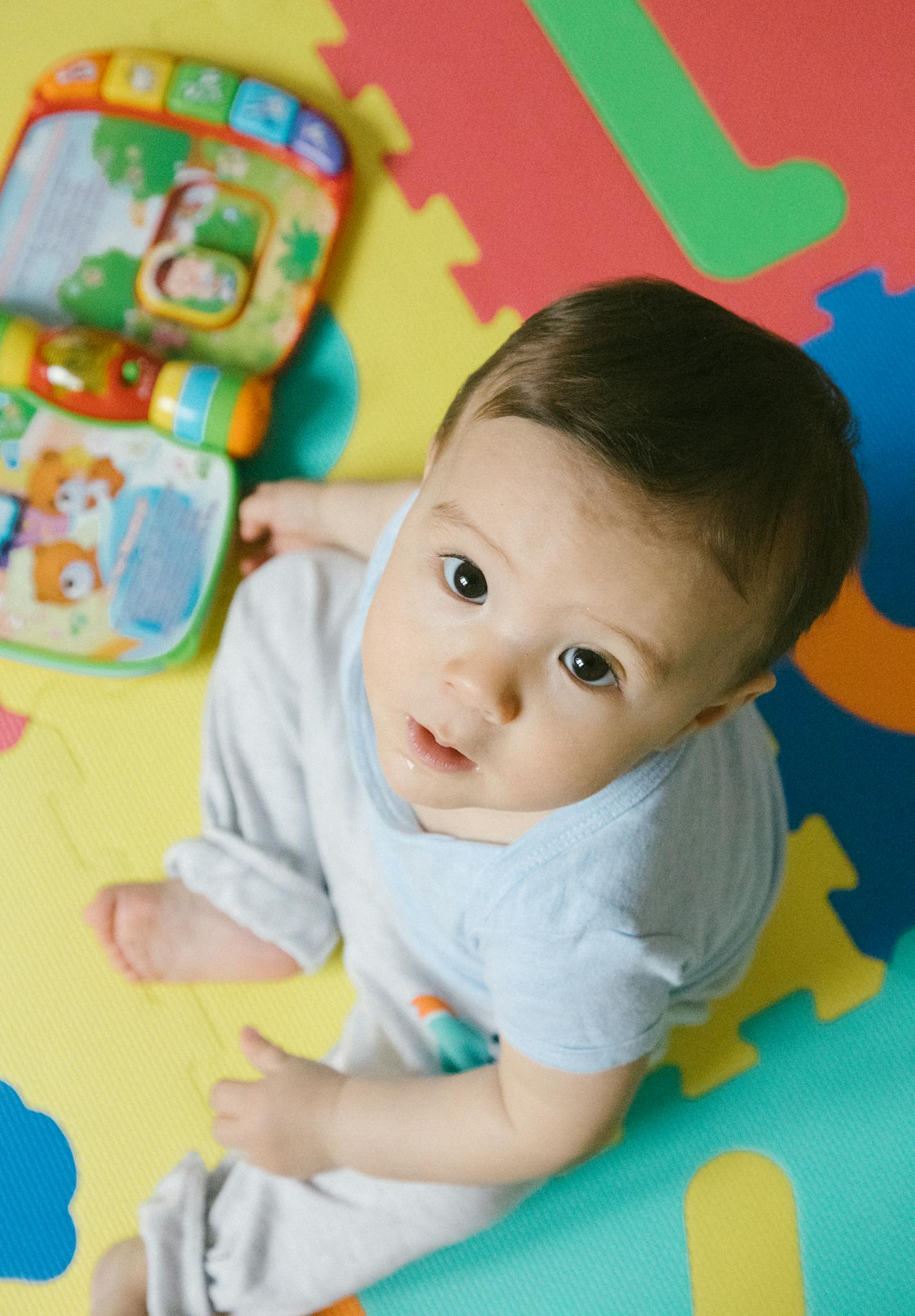 Cute baby sitting on a colorful puzzle mat, looking up with innocence.